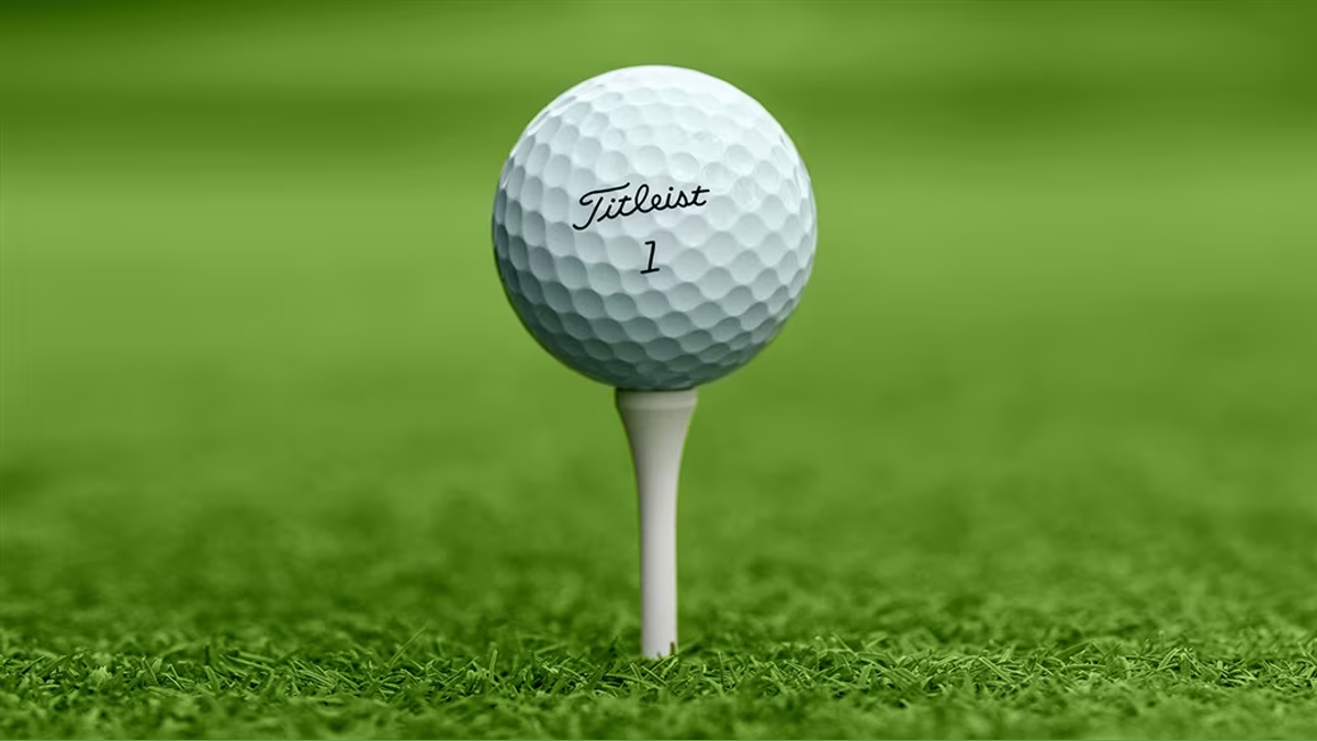 A golf ball resting on a tee over closely cut green grass.